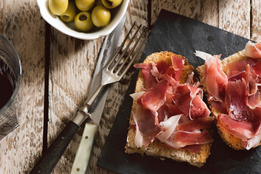 dos pequeñas tostas de jamón junto a un platito de aceitunas